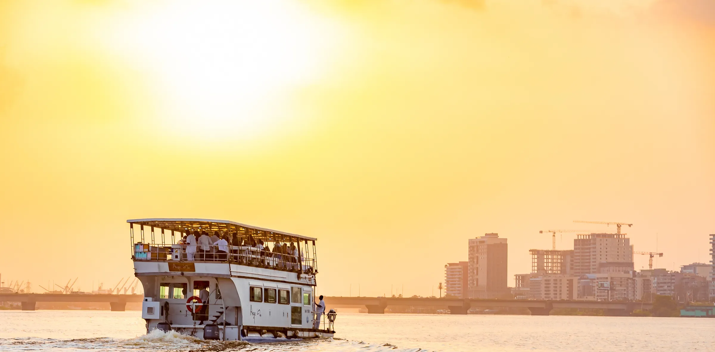 Le double-pont Sunset Tour en navigation sur la lagune Ébrié au coucher du soleil, devant le skyline d'Abidjan